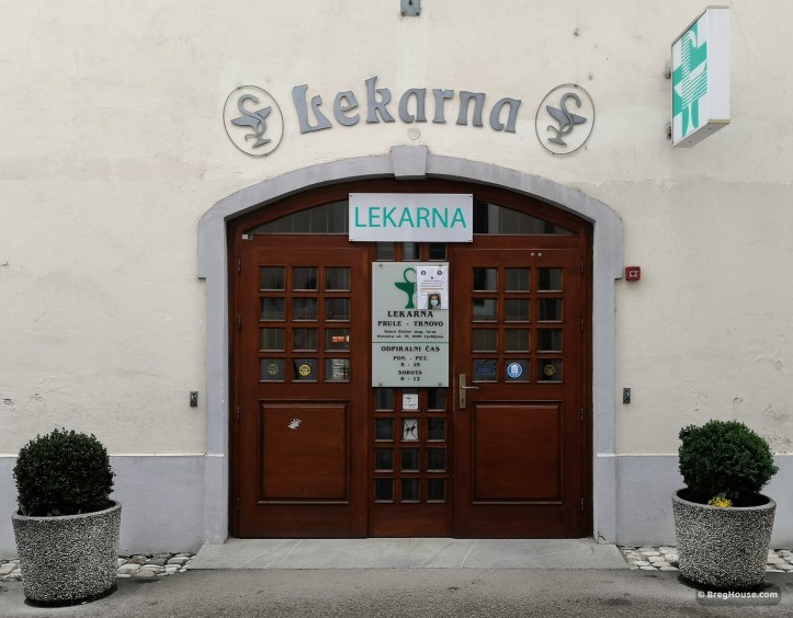 Lekarna (pharmacy) door in Ljubljana, Slovenia, flanked by two potted plants.